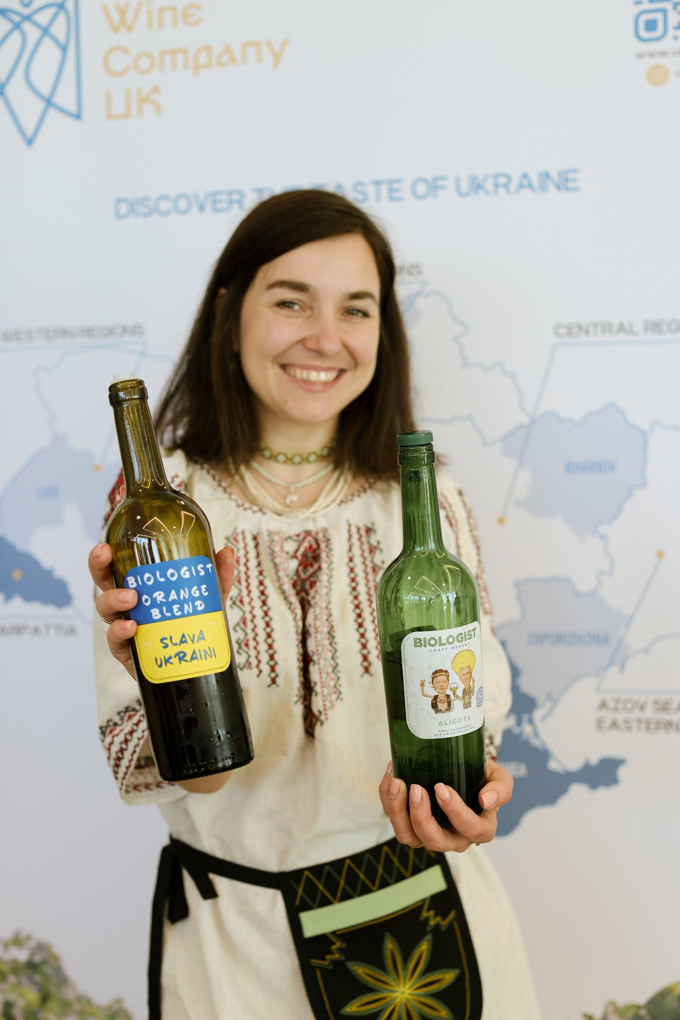 Woman holding two bottles of orange wine with a map and branding in the background